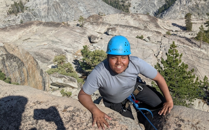 a person wearing a helmet smiles during a rock climbing trip for bipoc